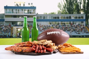 Rugby ball, snacks and bottles of beer on football field background